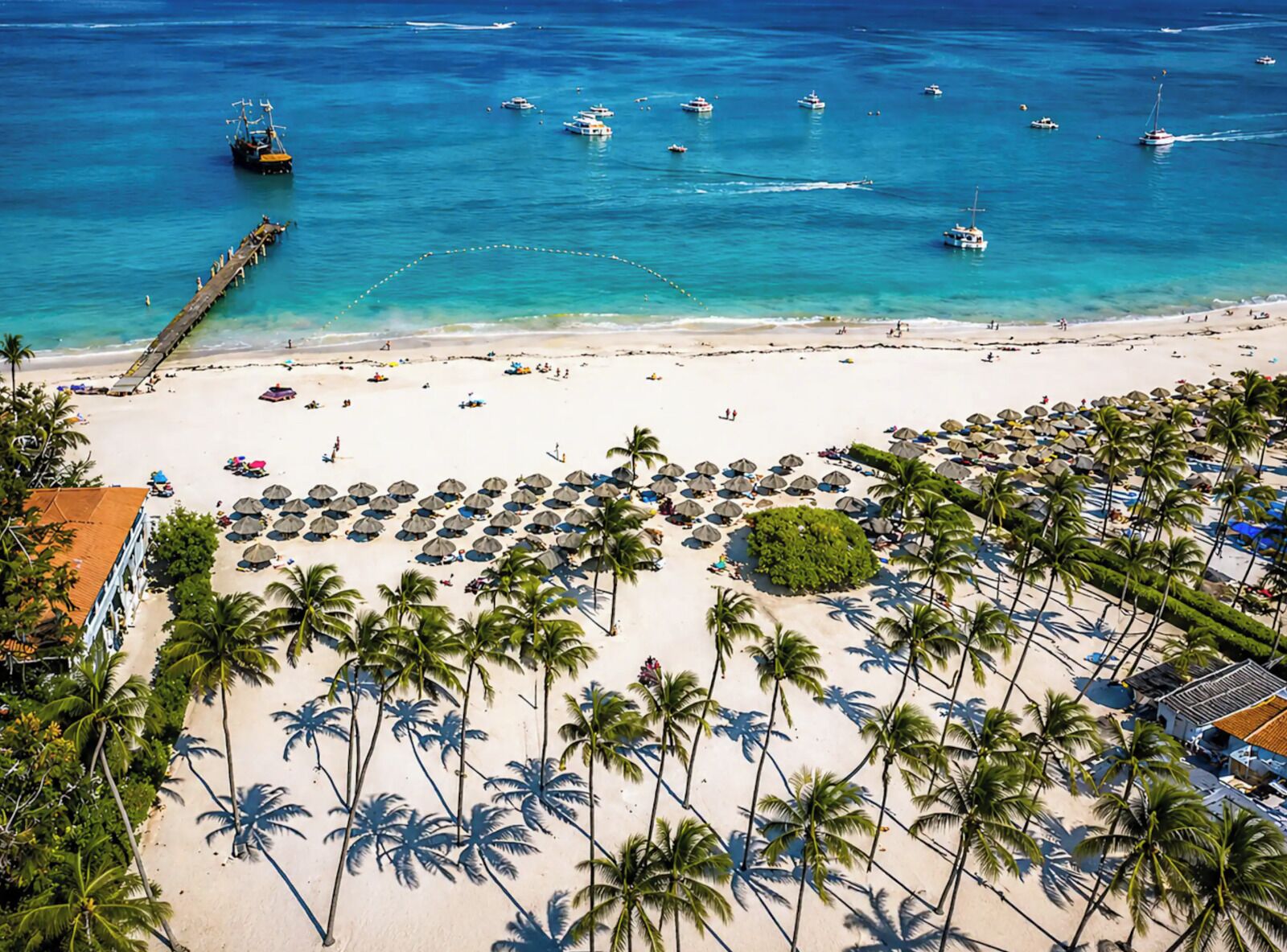 A beach with palm trees, a pier, and boats in the water.
