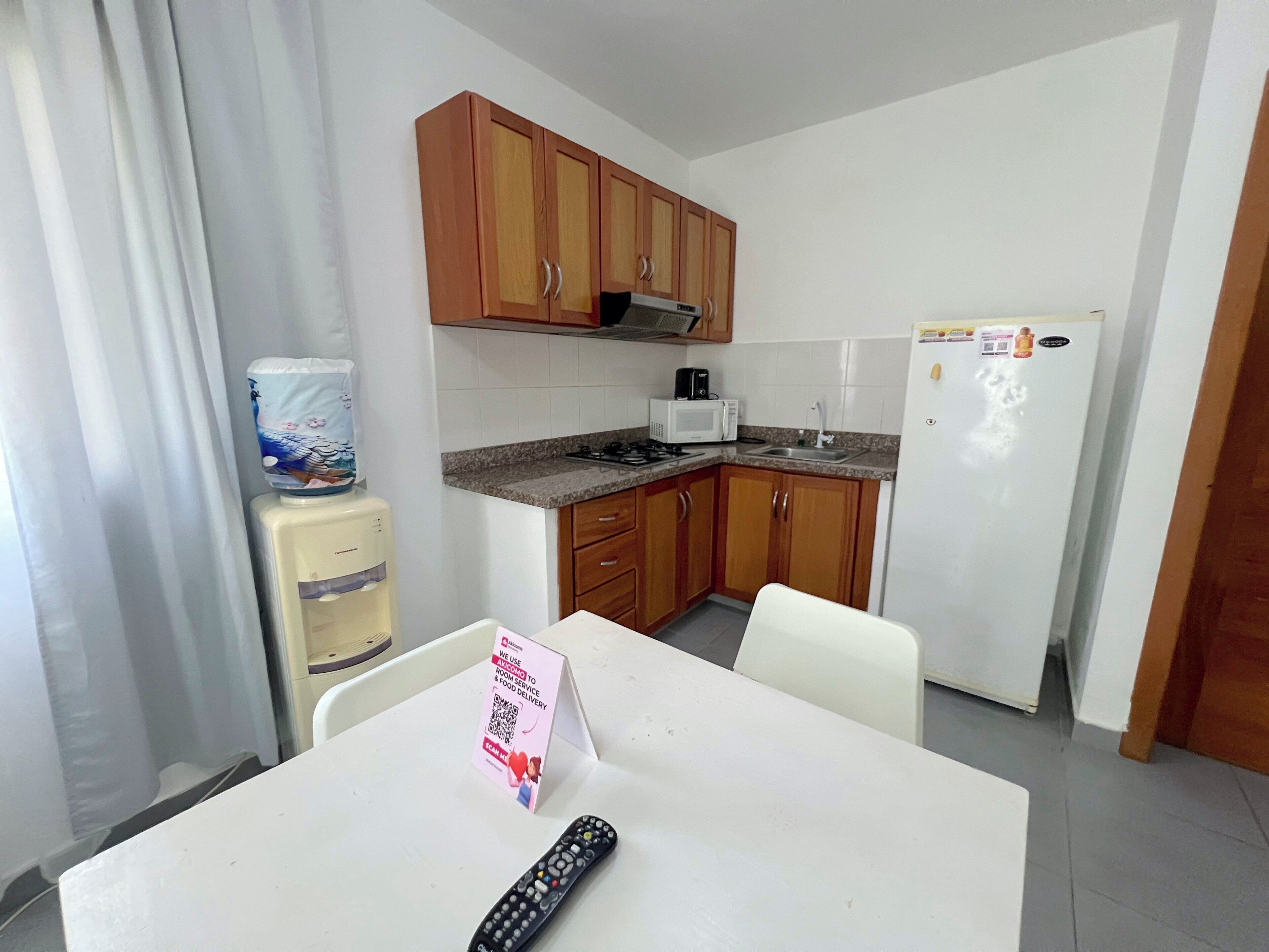 A compact kitchen with wooden cabinets, a microwave, a refrigerator, and a water dispenser.