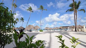 A beach with palm trees, thatched umbrellas, and a clear sky.