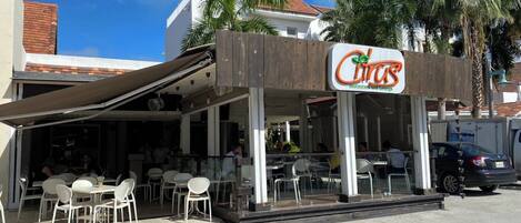 Restaurante con terraza, letrero y palmeras al fondo.