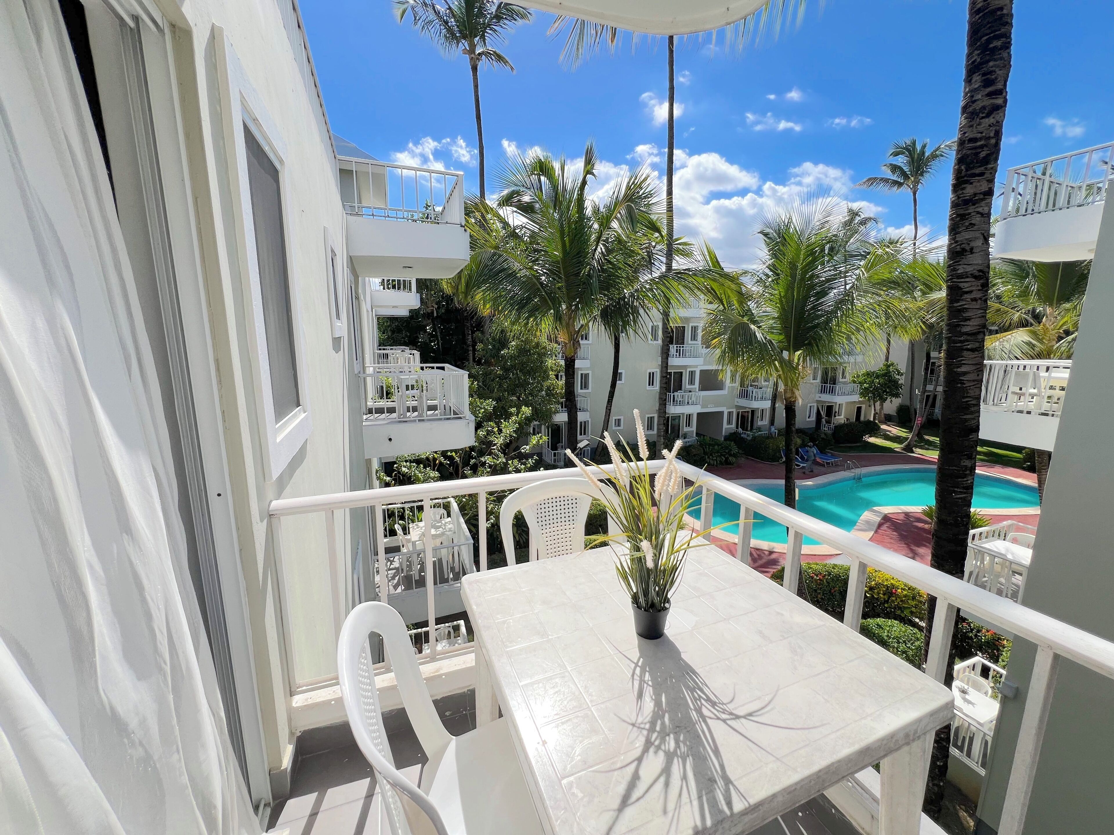 A balcony with a white table, chairs, and a potted plant.