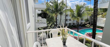 A balcony with a white table, chairs, and a potted plant.