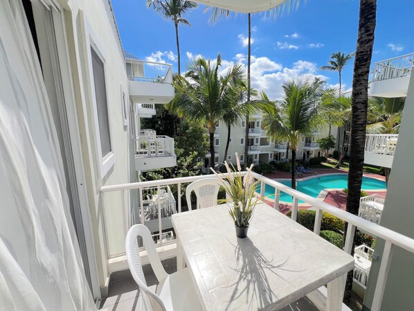 A balcony with a white table, chairs, and a potted plant.