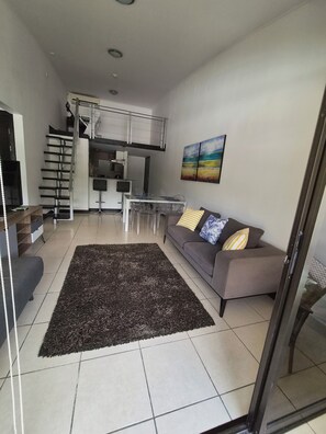 A modern living room with a grey sofa, a black shag rug, and a dining area with a glass table and chairs. - Aparmet, 2 bedrooms, gym, pool, restaurant, tennis, hot tub, Santa Ana, Río Oro (Río Oro)