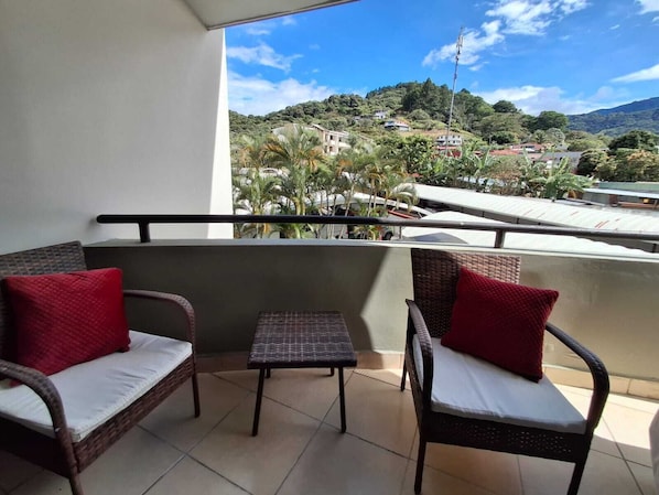 Ein Balkon mit Korbmöbeln und Blick auf eine hügelige Landschaft.