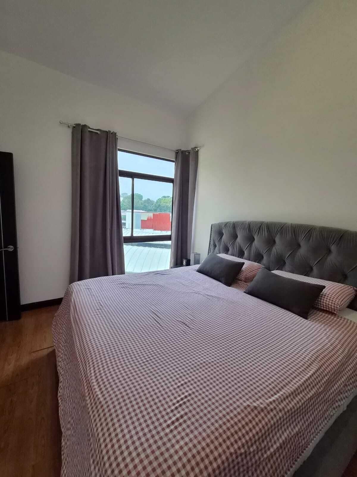 A bedroom with a large bed, a window with curtains, and a view of the outside.