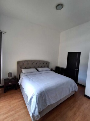 Quarto com cama grande, mesa de cabeceira, guarda-roupa e luz no teto.