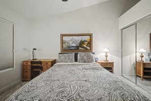 Een slaapkamer met een bed, een bureau, een stoel, een kaptafel, een spiegel en een schilderij aan de muur.