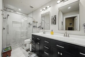 Een moderne badkamer met een douche in een glazen cabine, een wastafel met een grote spiegel en een toilet.
