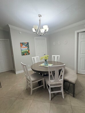 Ein Esszimmer mit einem runden Tisch, sechs Stühlen, einer Chandelierleuchtre und einer Wanddekoration zum Thema Florida.