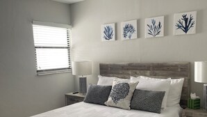 Ein Schlafzimmer mit einem Bettgestell aus Holz, einem Deckenventilator, einem Fenster mit Jalousien und Wandbildern.
