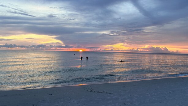 Ein Strand bei Sonnenuntergang, ruhige See und Fußabdrücke im Sand.