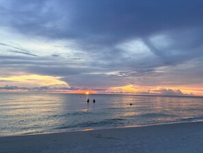 Ein Strand mit Sonnenuntergang, ruhiger See und Fußspuren im Sand.