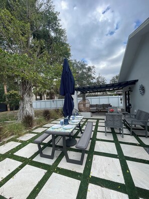 An outdoor patio with a table set for dining, surrounded by artificial grass and stone tiles. - Welcoming  bright 3-bedroom house in sunny Naples Park. (Naples)
