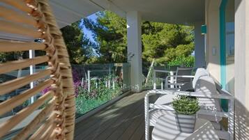 A covered outdoor seating area with a wooden deck, white furniture, and a potted plant.