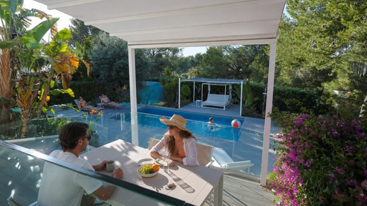 Un espace extérieur aménagé avec une véranda donnant sur la piscine, un espace de repos couvert et une végétation luxuriante.