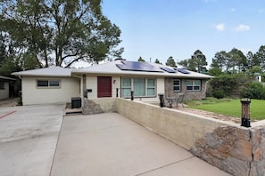 A single-story house with a stone retaining wall, a red door, and solar panels on the roof.