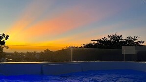 Sonnenuntergangblick vom Dach mit blauem Himmel, einem Pool und einer entfernten Baumgrenze.