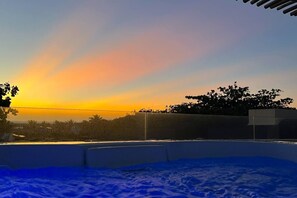 A sunset view from a rooftop with a clear sky, a pool, and a distant tree line. - Deluxe Villa Luz Do Mar, rooftop Jacuzzi, sea view (Jijoca de Jericoacoara)