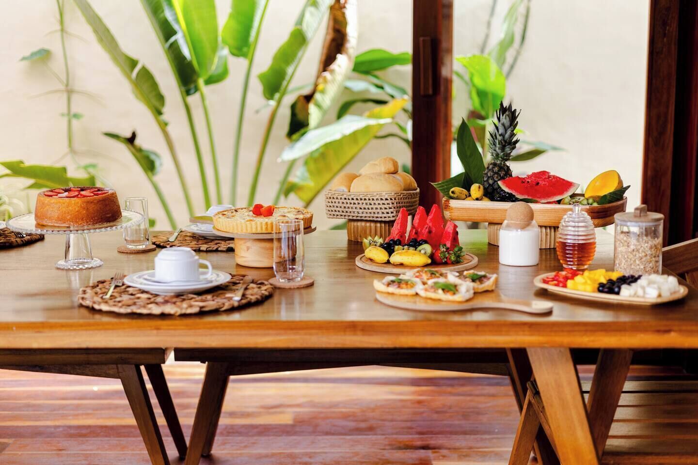 Uma mesa de jantar de madeira com diversos alimentos, incluindo um bolo, frutas e um copo de água.
