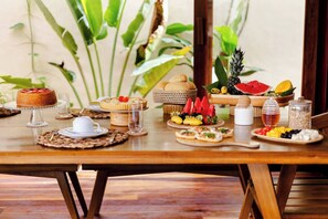A wooden dining table with various food items, including a cake, fruits, and a glass of water. - Deluxe Villa Luz Do Mar, rooftop Jacuzzi, sea view (Jijoca de Jericoacoara)