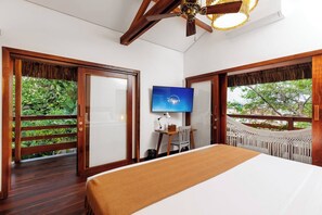 A hotel room with a bed, a television, a desk with a chair, and a balcony with a view of greenery. - Deluxe Villa Luz Do Mar, rooftop Jacuzzi, sea view (Jijoca de Jericoacoara)