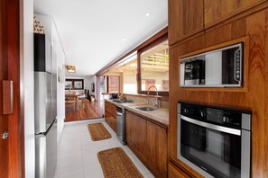 A modern kitchen with wooden cabinets, stainless steel appliances, and a dining area with a wooden table and chairs. - Deluxe Villa Luz Do Mar, rooftop Jacuzzi, sea view (Jijoca de Jericoacoara)