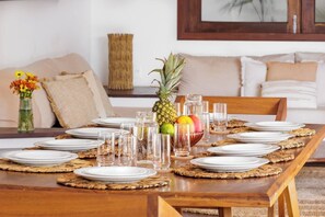 Una mesa de comedor dispuesta con platos, vasos y un centro de mesa con frutas y una piña.