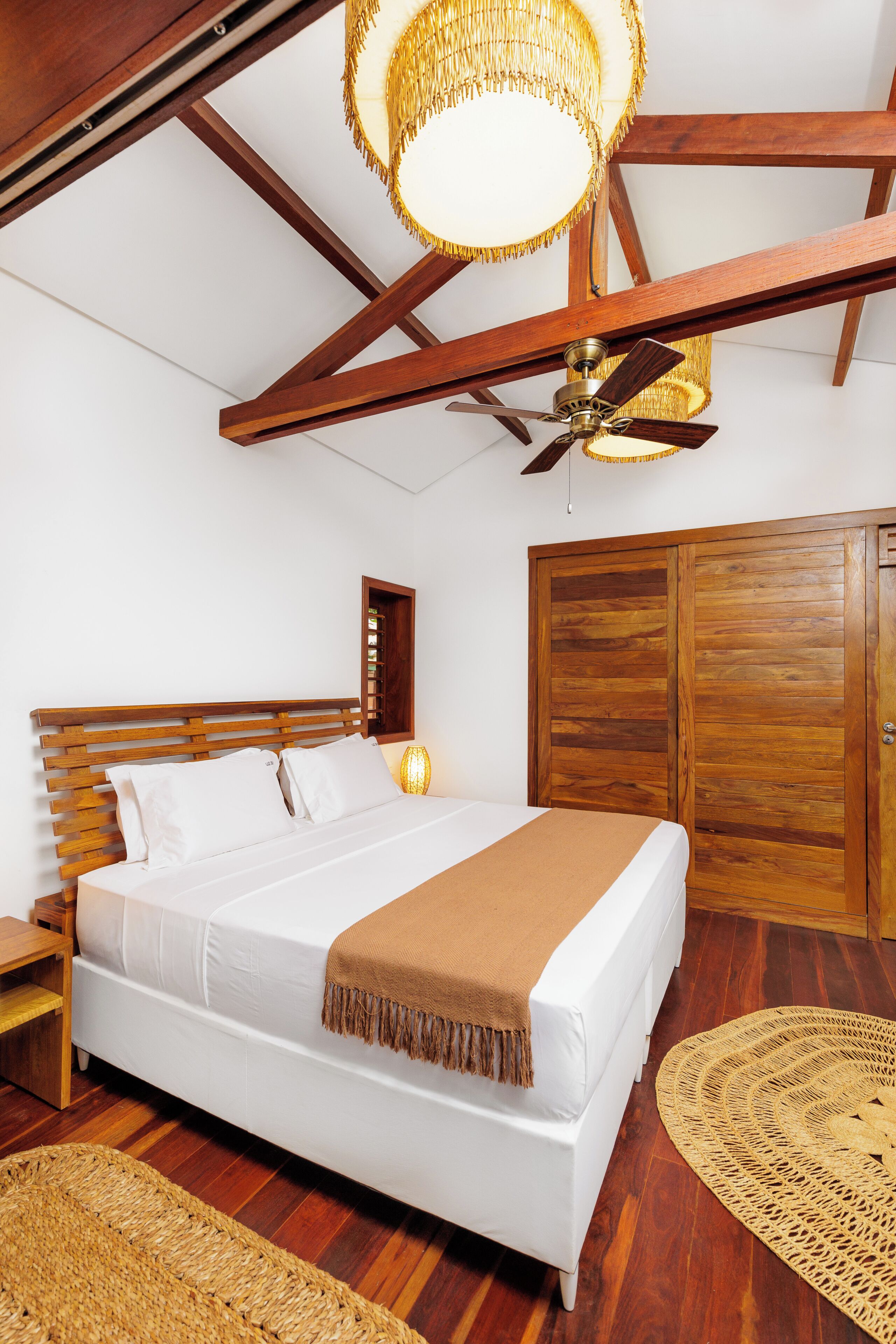 Quarto com cama de madeira, ventoinha no teto e um guarda-roupa de madeira grande.