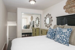 Une chambre à coucher comprenant un lit, deux miroirs décoratifs, une armoire et une porte donnant sur une autre pièce.