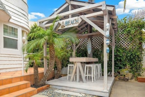 Eine Holz-Pergola mit einem Schild, auf dem 'Beach' steht, und einem Tisch mit Stühlen darunter.