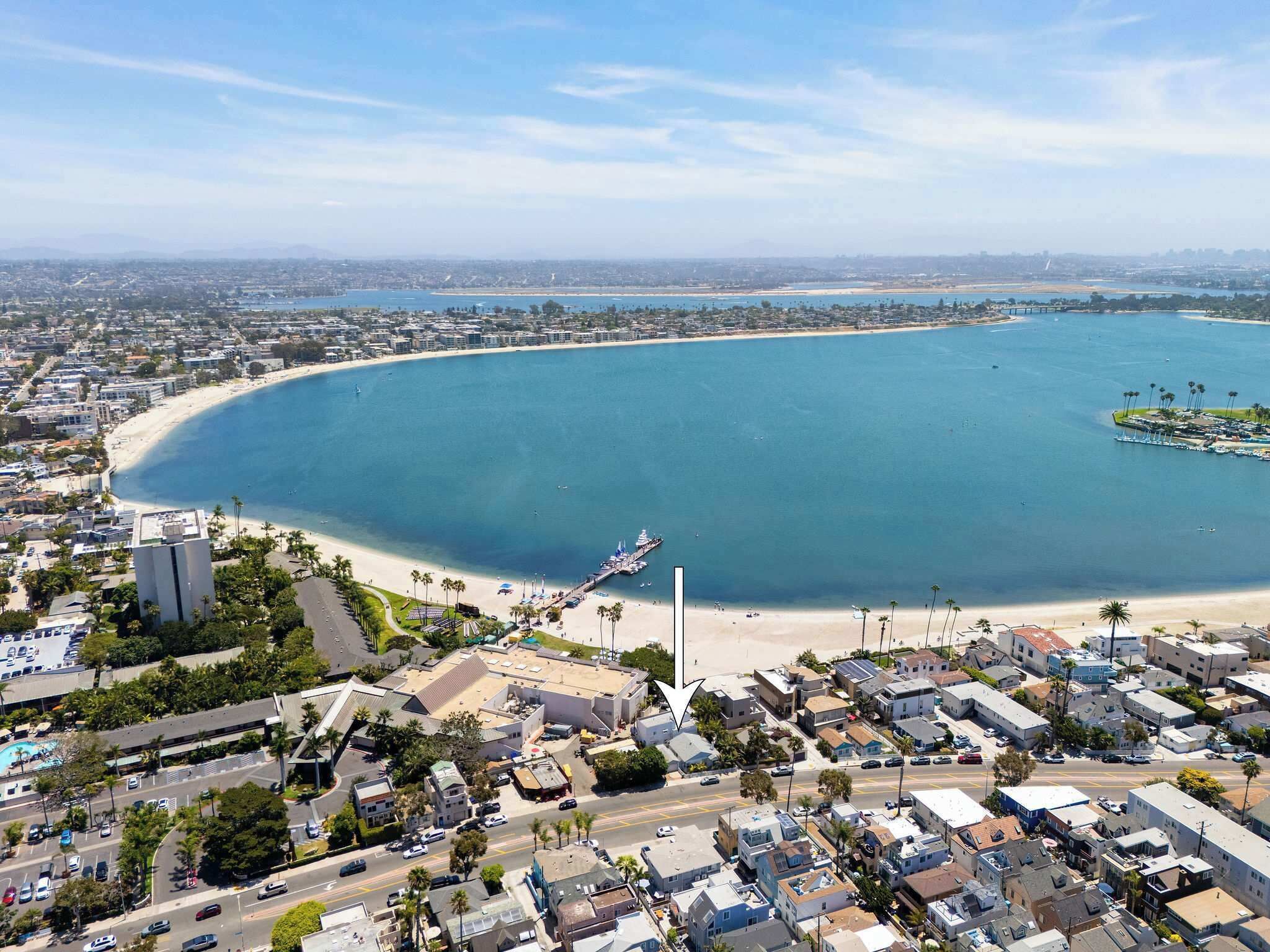 Eine Luftaufnahme einer Küstenstadt mit einer weiten Bucht, einem Strand und einem Yachthafen.