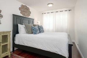 Una camera da letto con un letto, un comodino, un cartello appeso al muro e una finestra con tende.