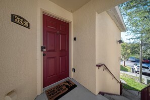 A red door with a doormat, a mailbox, and a street view.