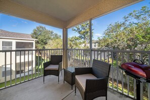 Ein überdachter Balkon mit Korbmöbeln und einem Grill.
