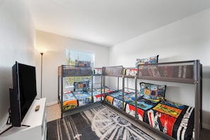 A room with bunk beds, a television, and a window with blinds.