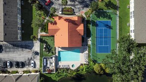 Vue aérienne d’une propriété résidentielle dotée d’une piscine, d’un court de tennis et d’un jardin clôturé.