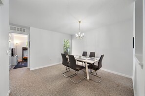Un espace repas comprenant une table et des chaises, un lustre et un sol recouvert d’une moquette.