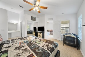 Une chambre à coucher comprenant un lit, un ventilateur de plafond, une télévision, une commode et une fenêtre avec des stores.