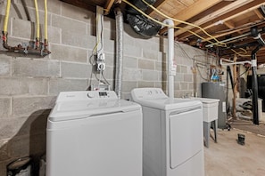 A laundry room with two front-loading washing machines, a water heater, and various pipes and hoses.