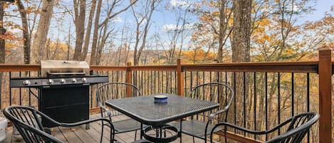 An outdoor deck with a grill, metal chairs, and a table.