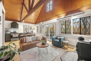 A spacious living area with a high ceiling, a kitchen, and large windows with diamond-patterned glass.