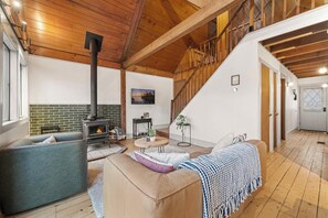 A spacious living area with a fireplace, a sofa, a coffee table, and a staircase leading to an upper level. - Cozy Masthope Chalet on 2 Private Wooded Acres w/ Grill, Fire Pit & Pet-Friendly (Lackawaxen)