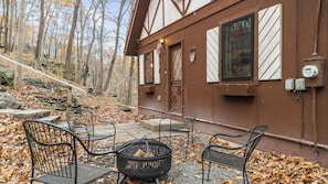 A cabin with a stone staircase leading to a wooden door, a fire pit with logs, and a bench.