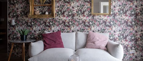 A living room with a floral wallpaper, a sofa, a small side table, and a decorative mirror.