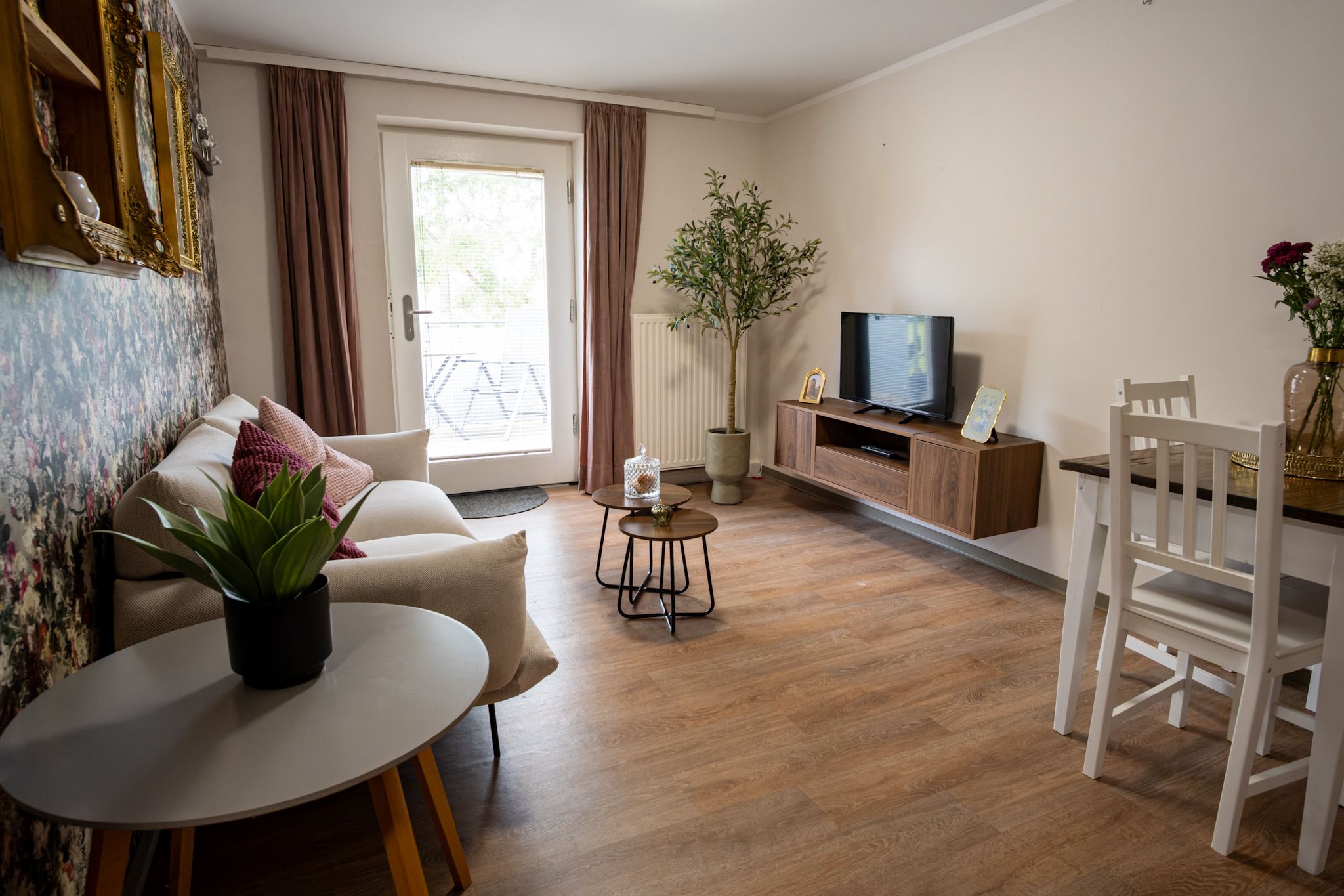 A living room with a sofa, a coffee table, a TV, a dining table with chairs, and a potted plant.