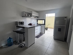 A compact kitchen with a built-in microwave, a small island with stools, a refrigerator, and a window providing natural light. - Modern Apartment in Querétaro | Capital Sur Residential Complex - Security | Wi-Fi - Smart TV (Capital Sur)