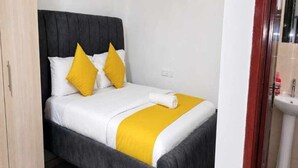 Ein Bett mit grauem Kopfteil, weißer Bettwäsche und zwei gelben Kissen.