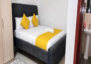 Ein Bett mit grauem Kopfteil, weißer Bettwäsche und zwei gelben Kissen.