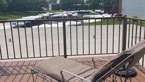 A deck with a cushioned chair and a metal table, overlooking a parking area with boats and a building in the background. - Anchor Stay!  Condo w/larger deck overlooking harbor, sleeps up to 6 (Clear Lake)